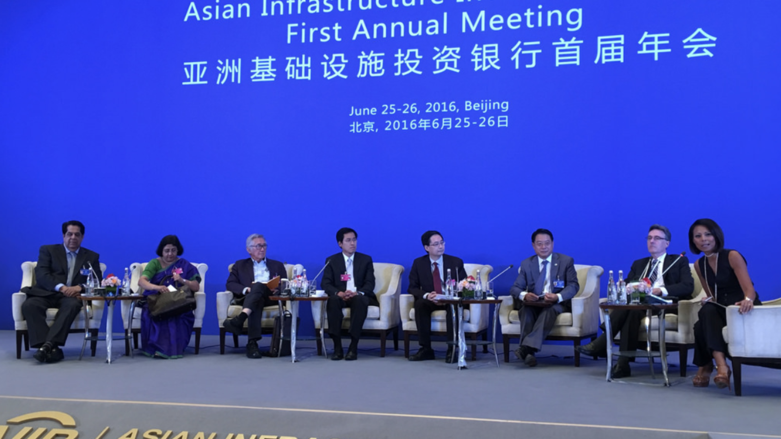 A panel of people sit on a stage in front of a screen that reads, &quot;Asian Infrastructure Investment Bank First Annual Meeting.&quot;