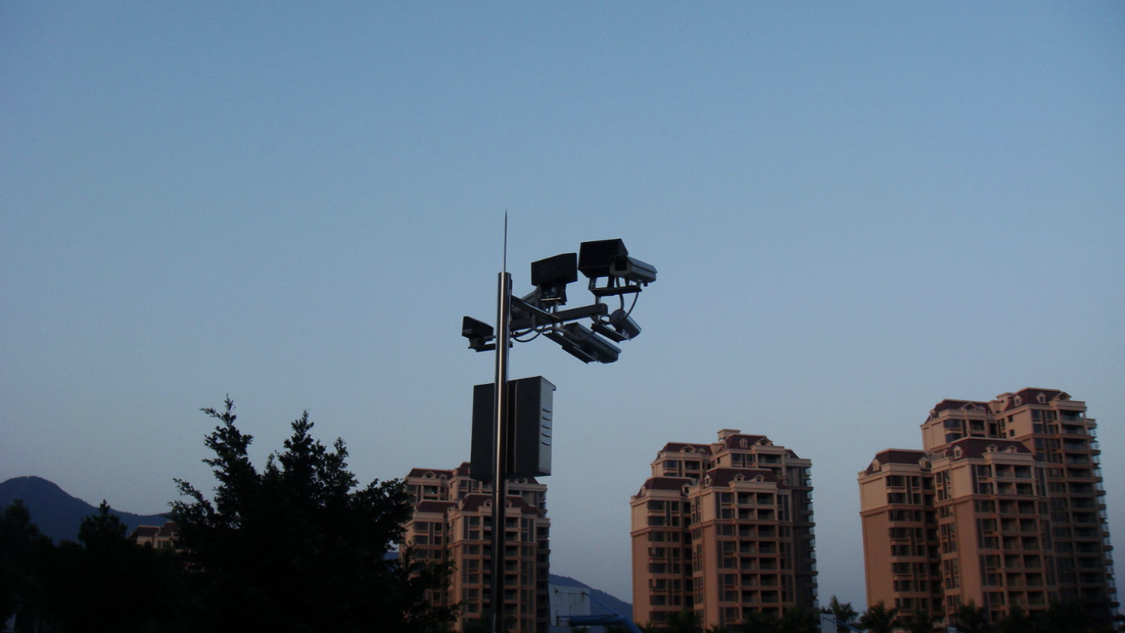 A group of large, modern buildings sit in the shadow, dark and without lights on.