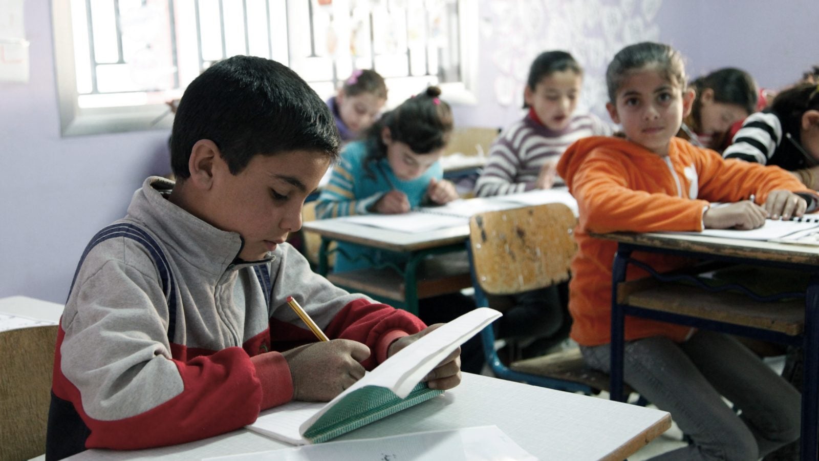 A Syrian student writes in a book in a classroom