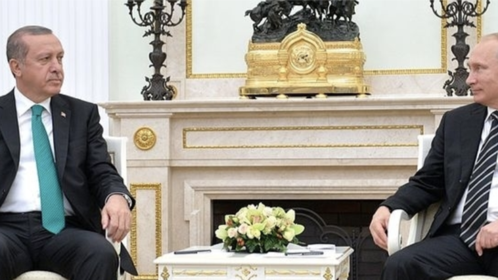 Putin and Erdogan sit in chairs in front of an ornate fireplace.