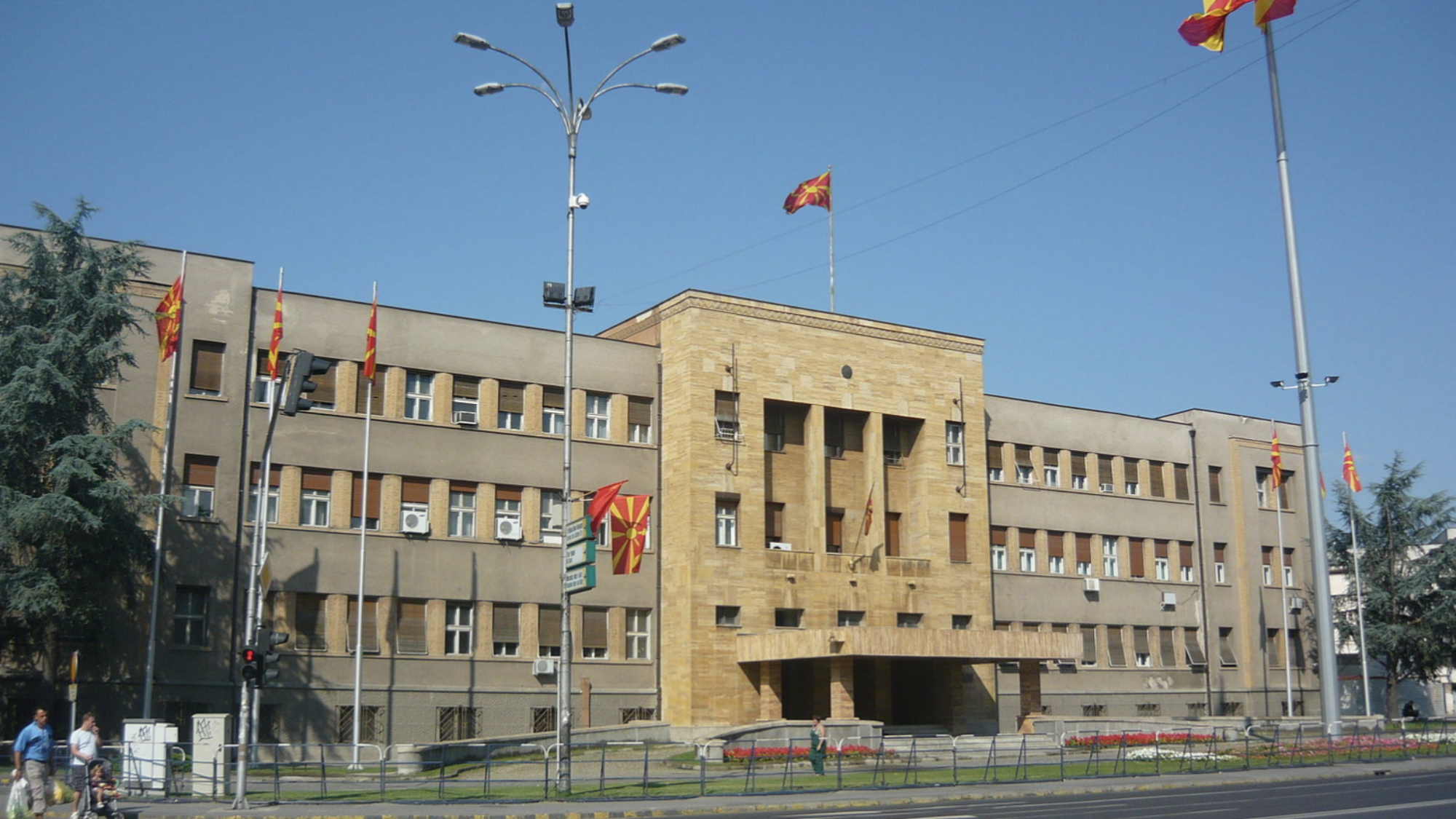 A photo of the front of the Macedonian parliament building, with the Macedonian flag flying out front