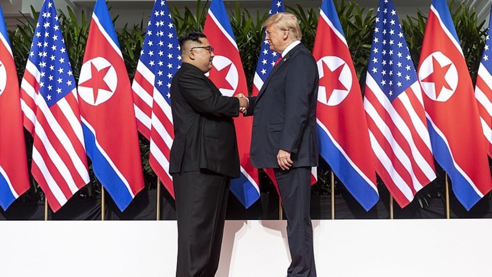 Donald trump and Kim Jong Un shanking hands in front of US and North Korean Flags