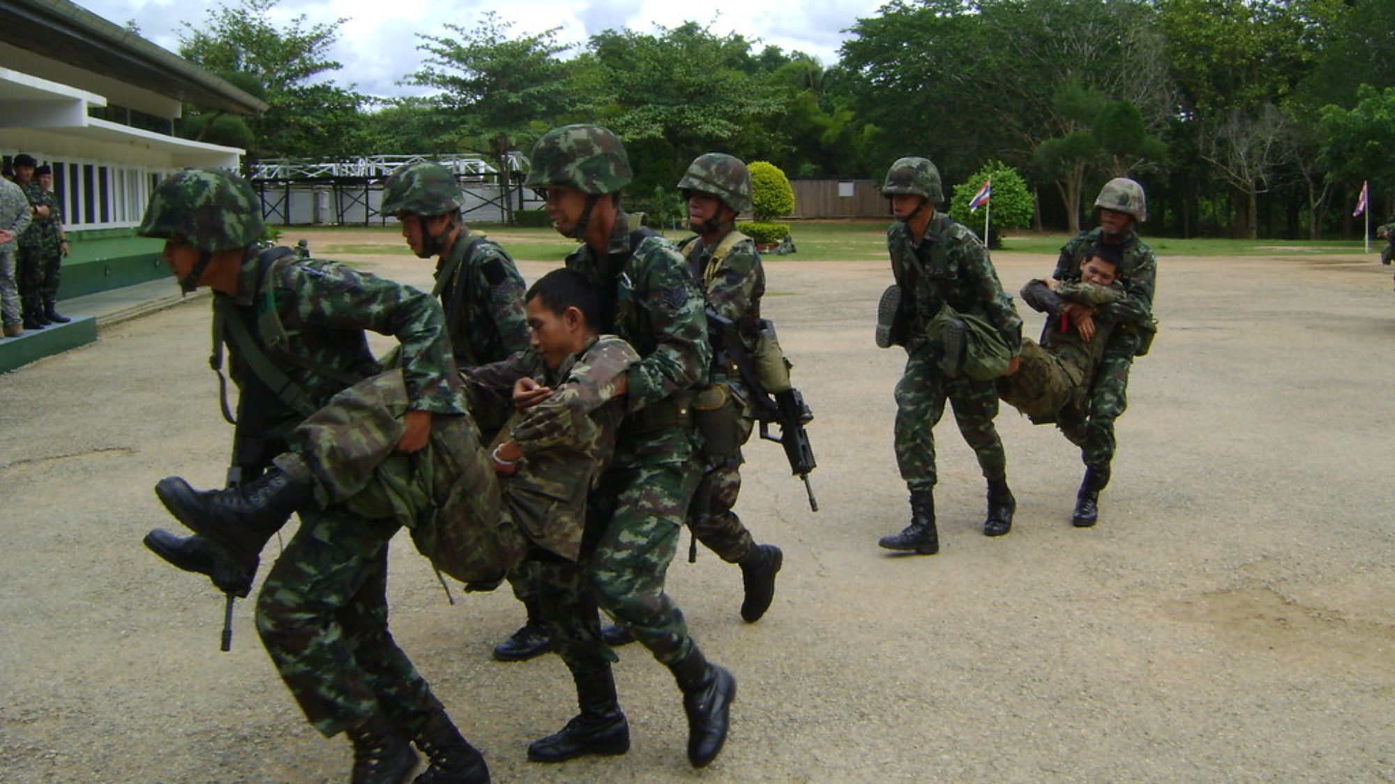 Thai soldiers practicing counterinsurgency training. Several men in Thai military uniform carrying another man in uniform.