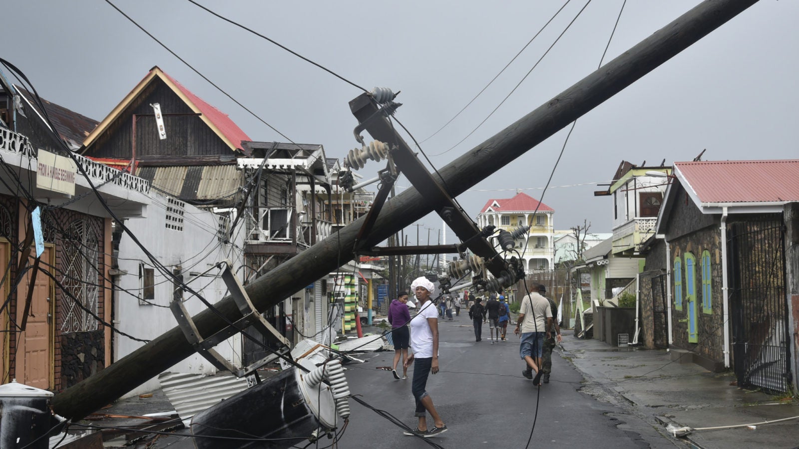 A fallen over telephone pole following natural disaster with people on the streets