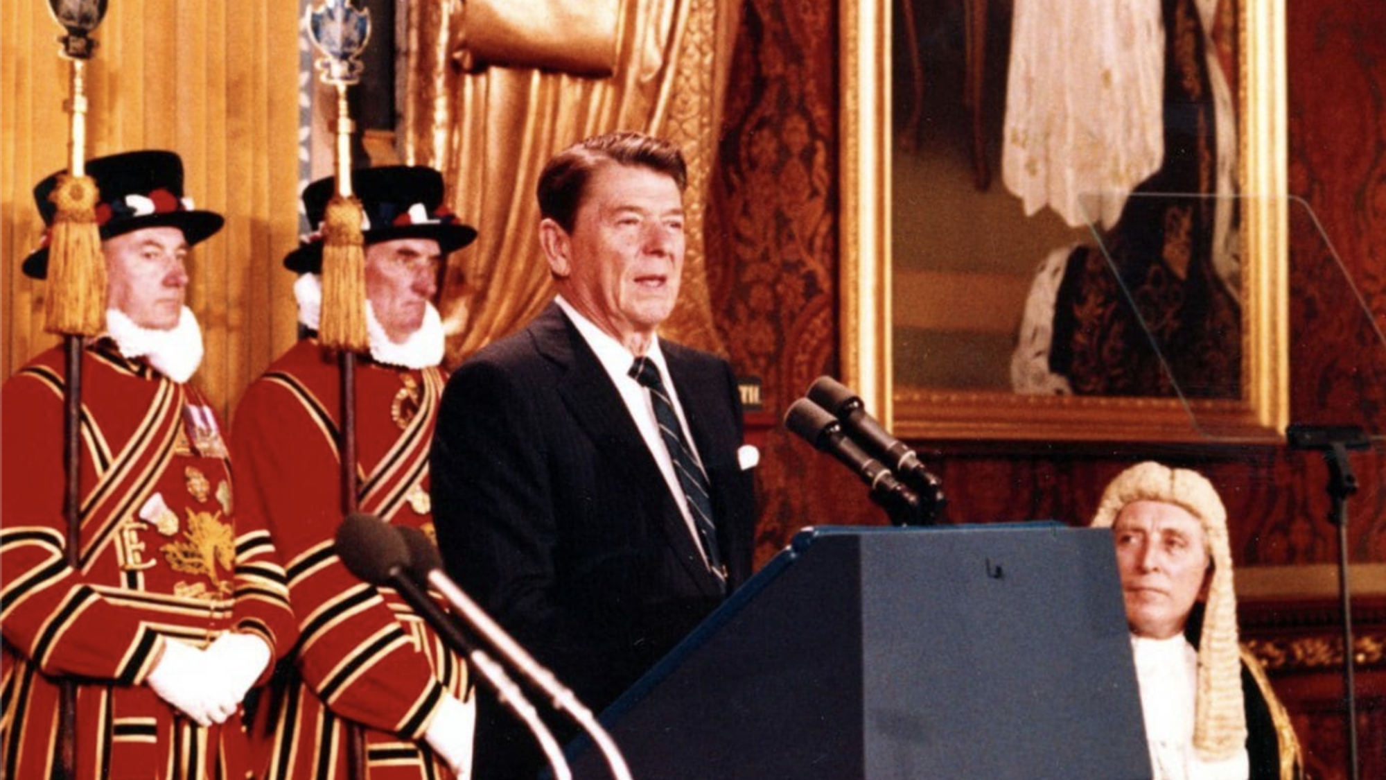 Ronald Reagan is standing at a podium and addresses the British parliament.