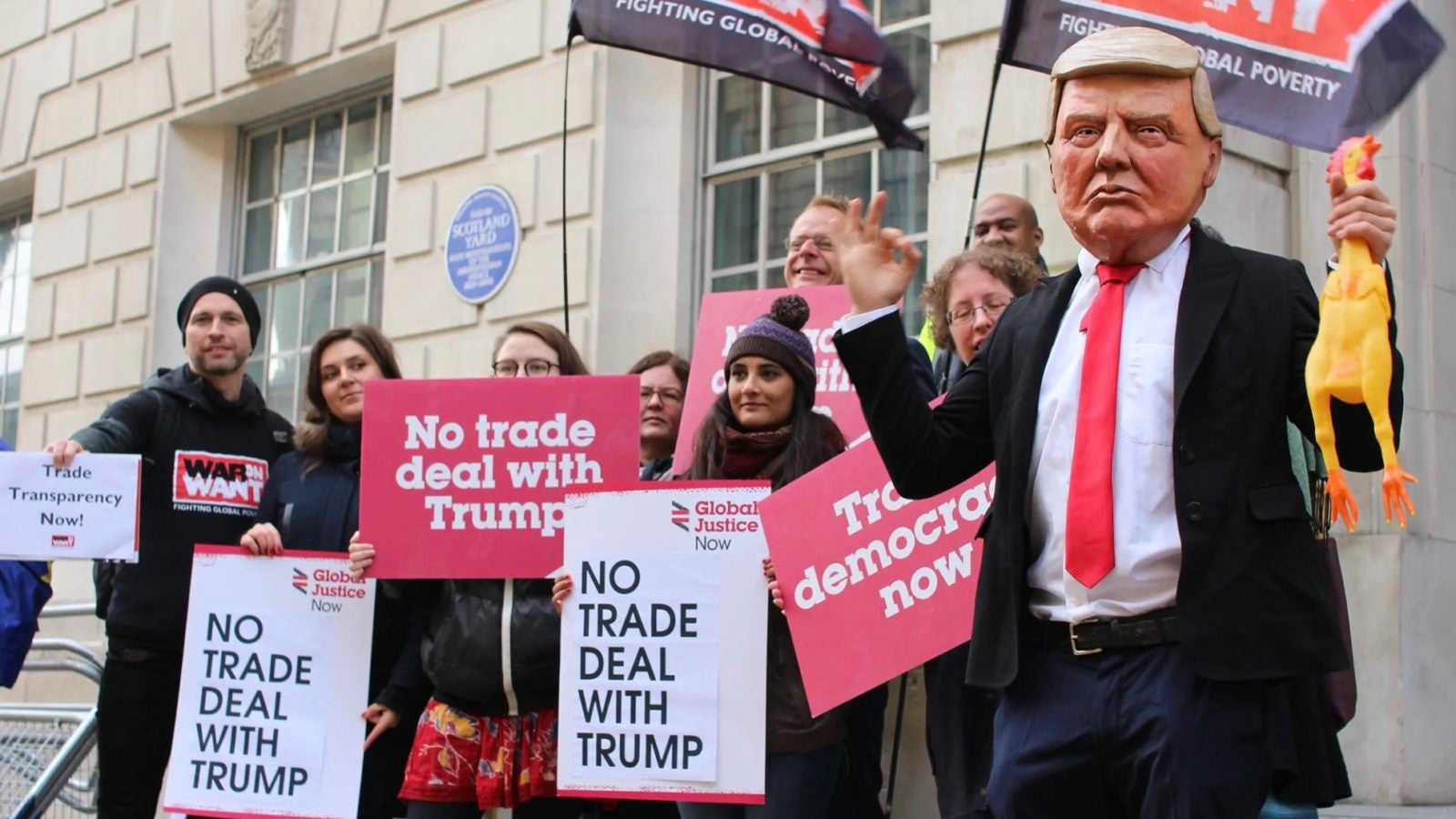 People standing outside of a building with banners and face masks protesting trump policy