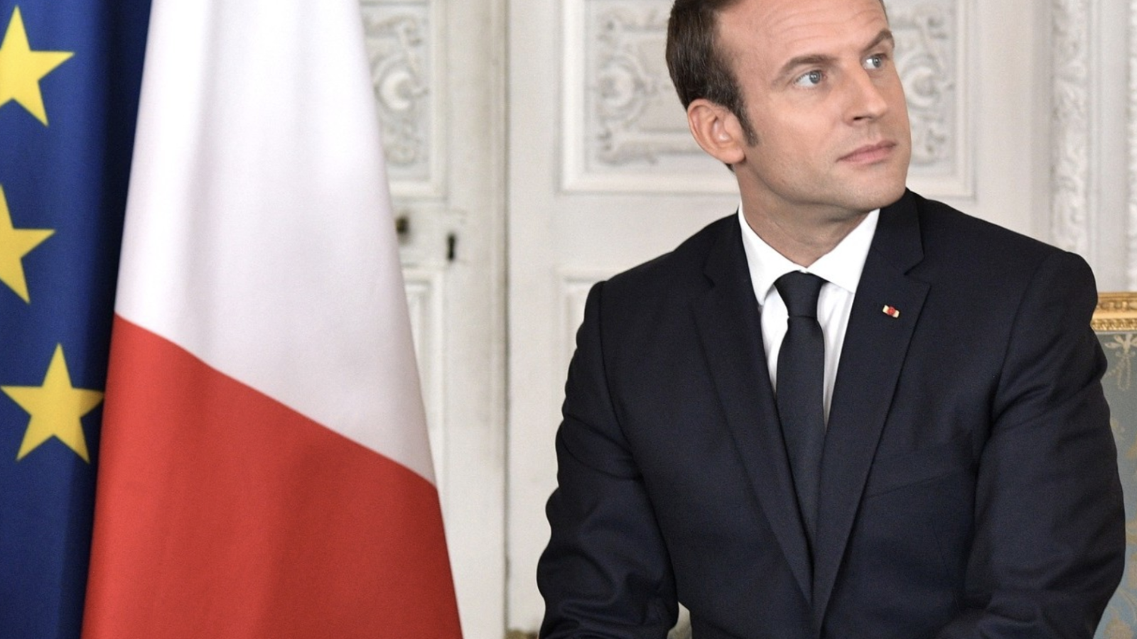 Emmanuel Macron sits in front of a French flag