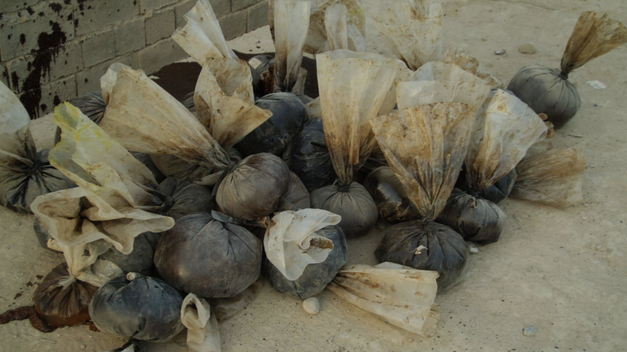 A pile of drug balloons sits on a dirt floor.