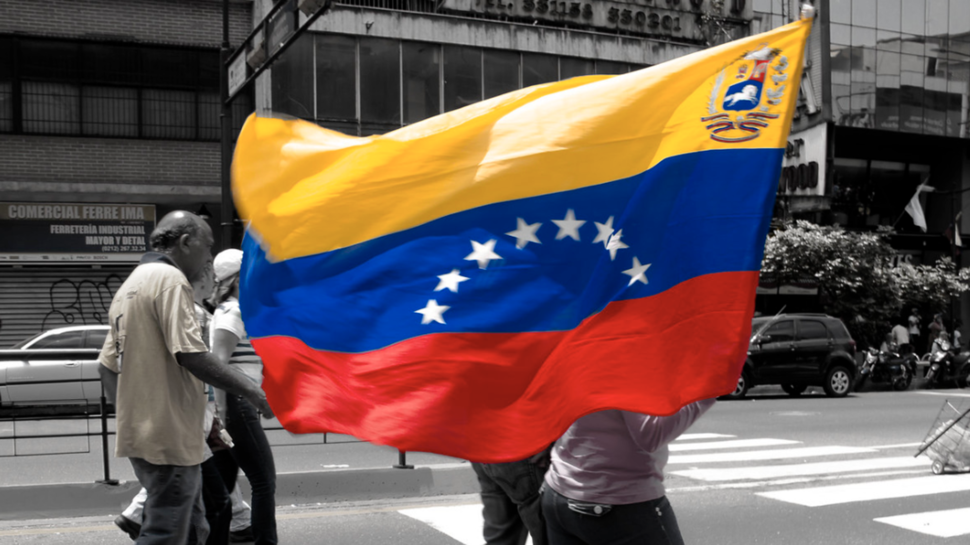A person walks down the middle of a street carrying the Venezuelan flag.
