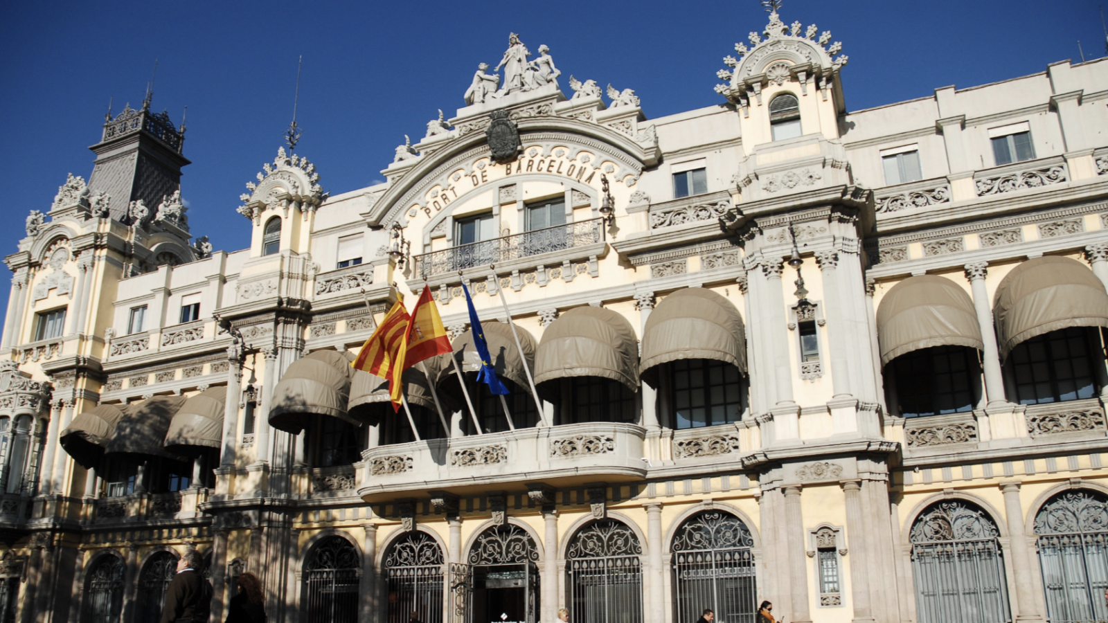 An ornate stone building with the flags of Catalonia, Spain, and the EU on the front, and the words &quot;Port de Barcelona.&quot;