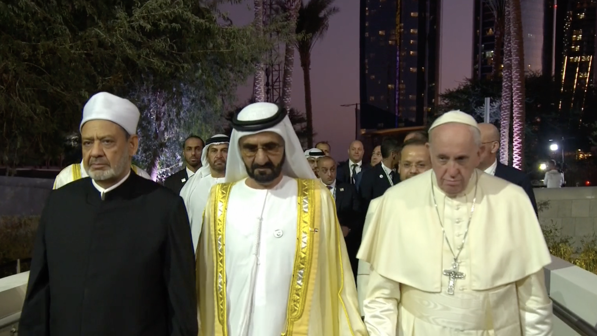 Sheikh Mohammed, Sheikh Ahmed el-Tayeb, and Pope Francis walk side-by-side in front of a crowd of people.