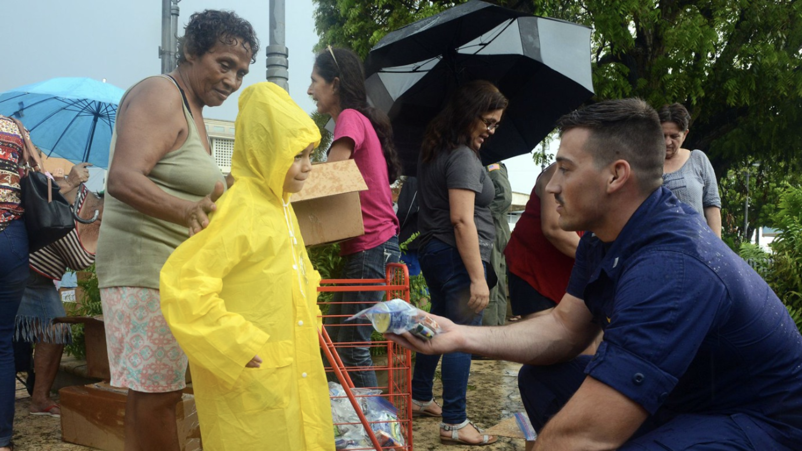 A man leans down to hand a small food and water package to a young girl.