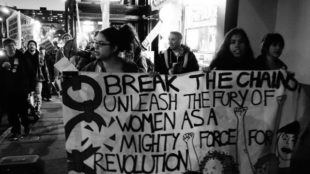 A group of women hold a sign that reads, &quot;Break the change, unlease the fury of women as a might force for revolution.&quot;