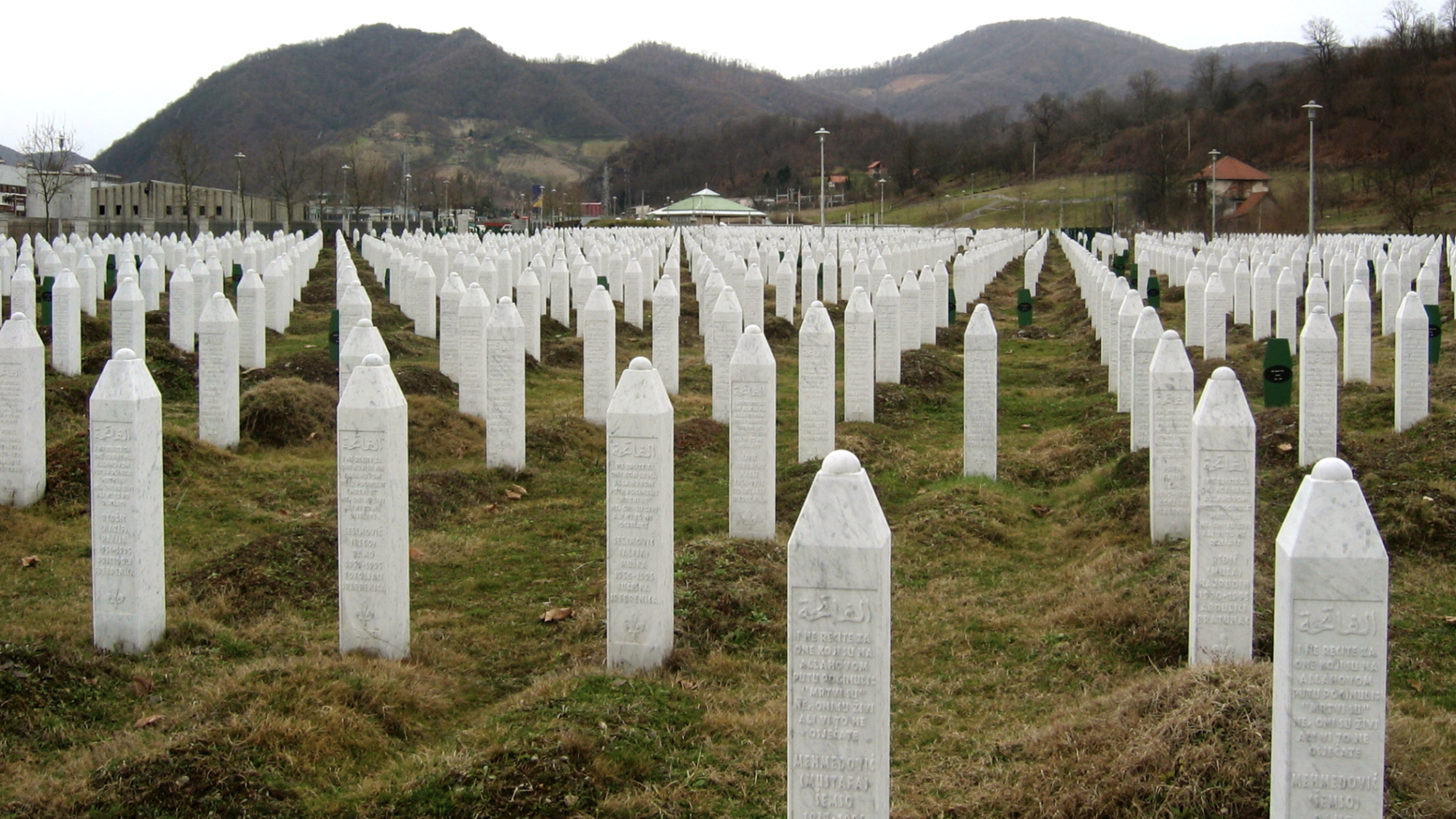 Rows of white, pillar-shaped gravestones are lined up in a field as part of a memorial to the Srebrenica genocide.