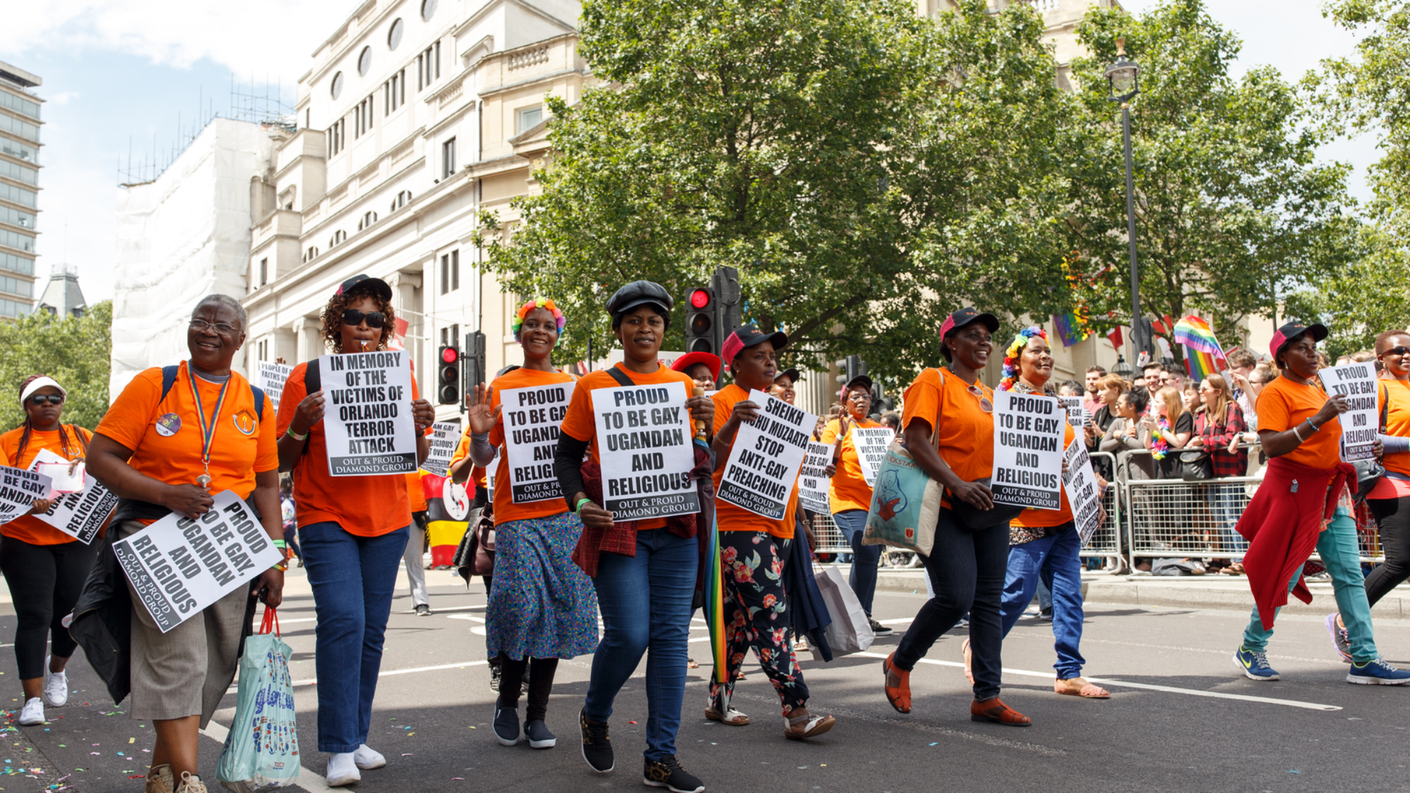 A line of people walking in a parade in Uganda holding pro-LGBTQ signs.