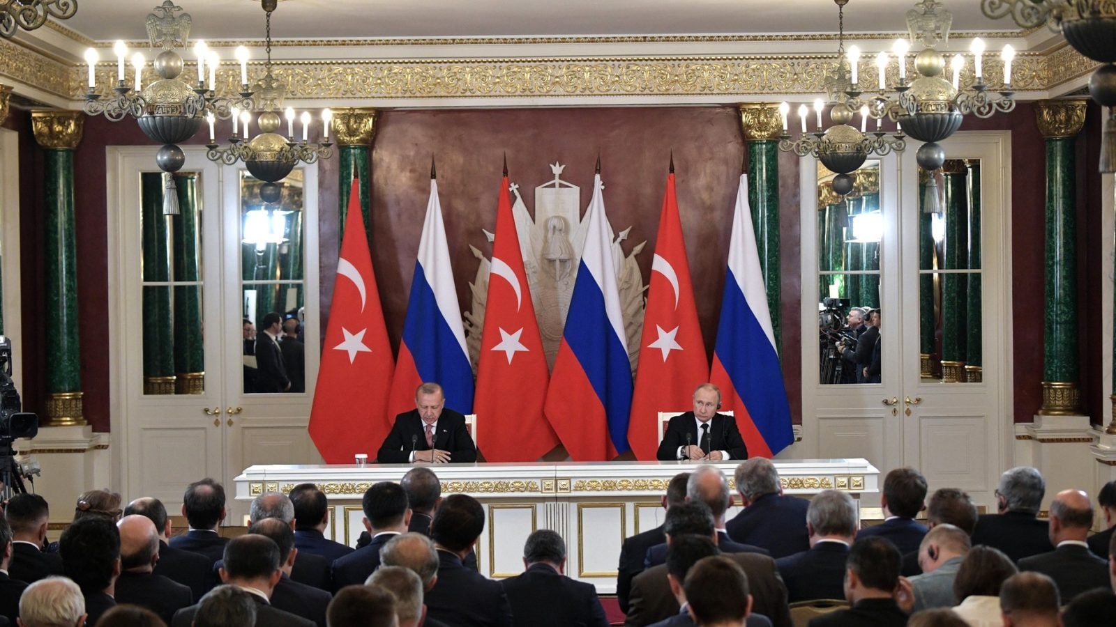 President Putin and President Erdogan sit at a table in front of the Turkish and Russian flags, in front of a room full of reporters.