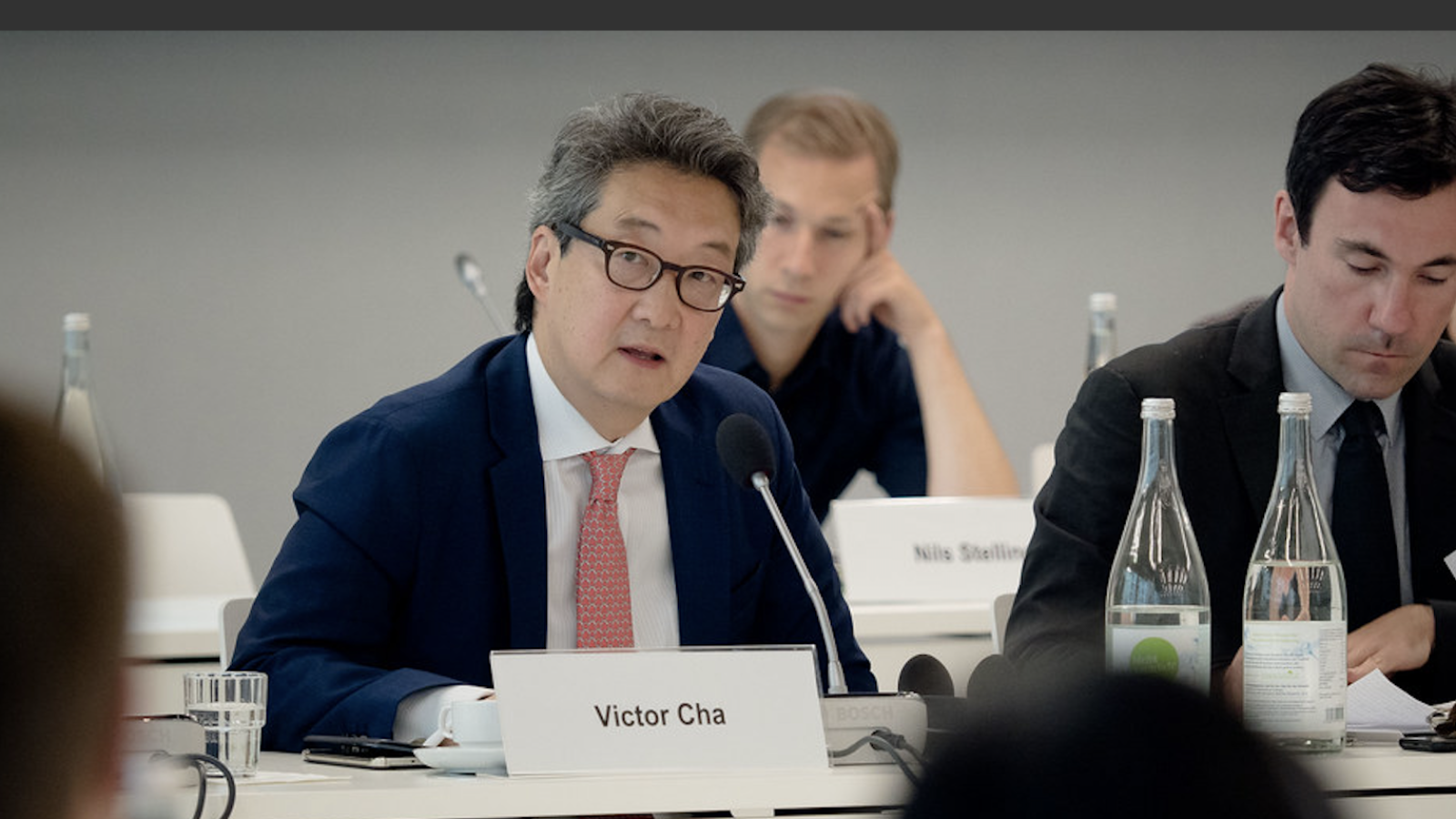 A man sits at a table behind a placard that reads &quot;Victor Cha.&quot;