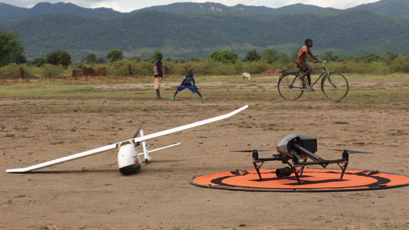 Two small drones sit rest on the dirt against the backdrop of mountains.