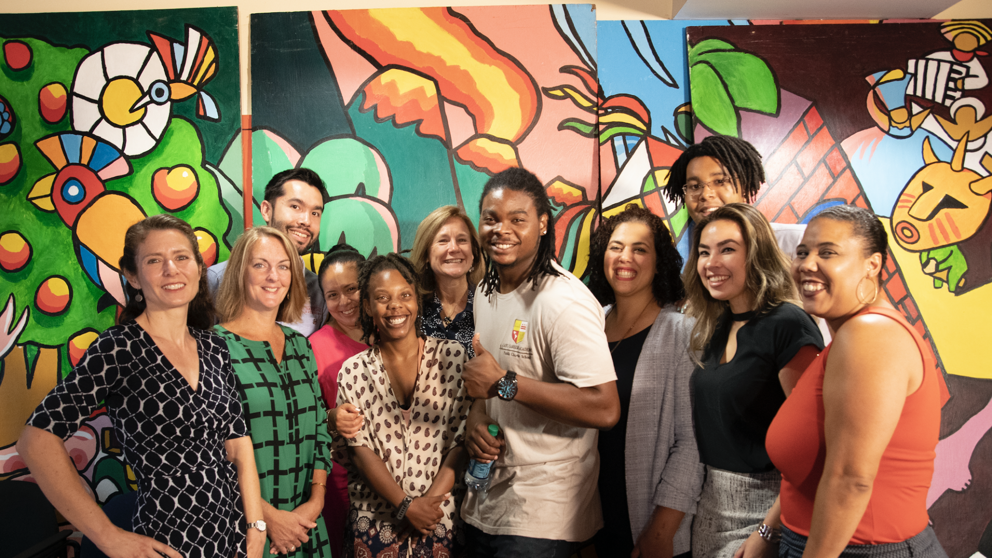 A group of people stand together smiling in front of a colorful mural.