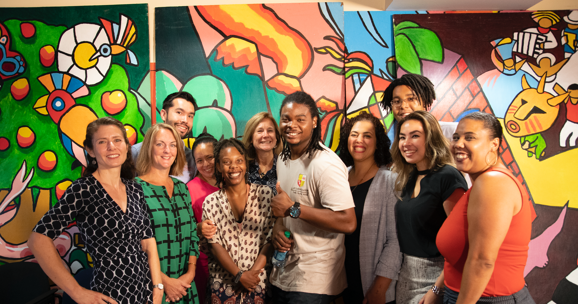 A group of people stand together smiling in front of a colorful mural.
