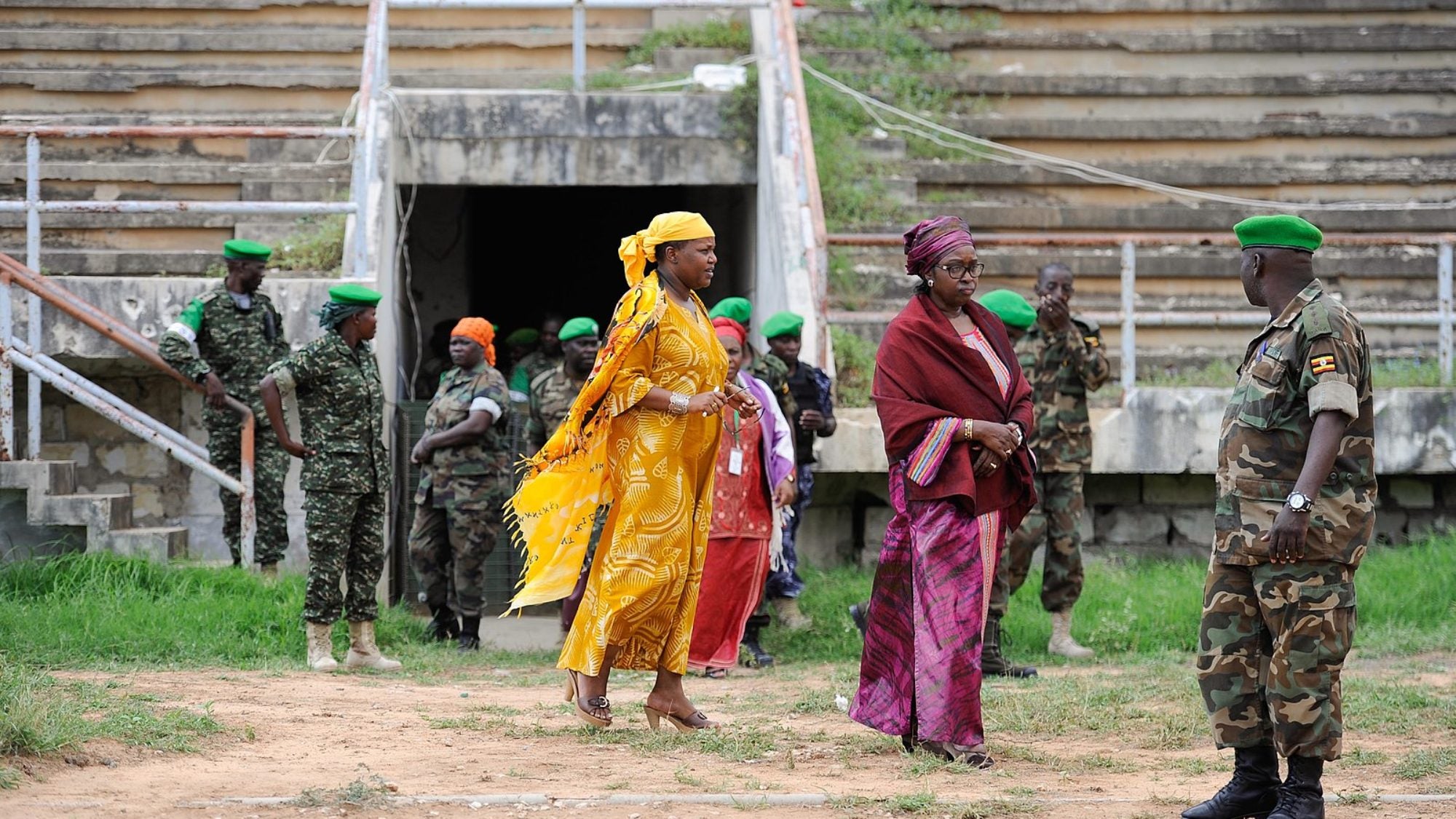 Three women in brightly colored clothing walk among soldiers in camouflage.