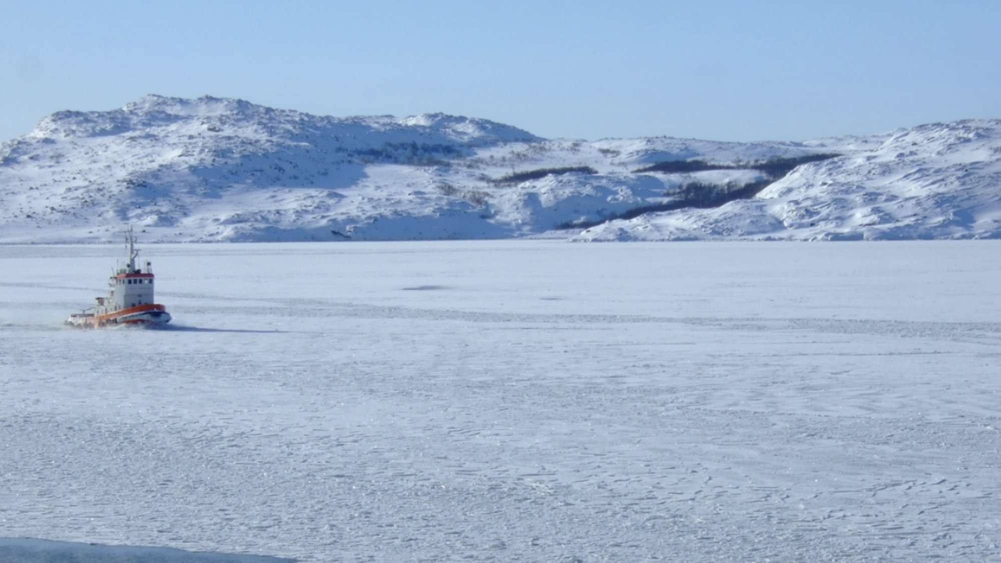 A small boat travels through icy water with glaciers in the background.