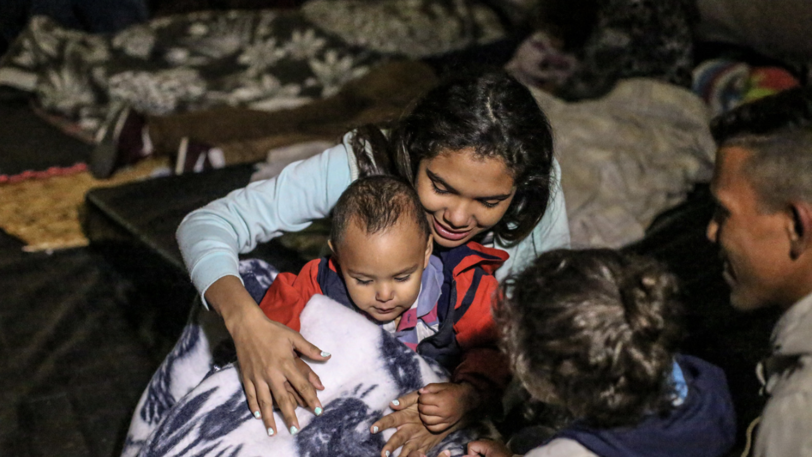 A Venezuelan mother and two of her children sit playing in a temporary shelter tent for migrants.