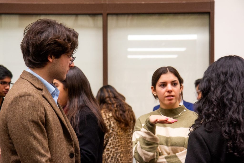 A group of students engages in a discussion. One student gestures while speaking, and others listen attentively in a casual setting.