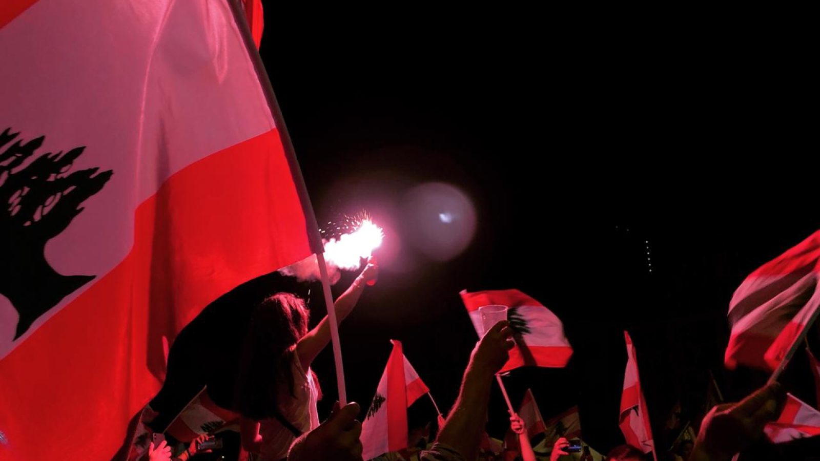 Flare shines light in group of passionate Lebanese protesters. Flags can be seen.