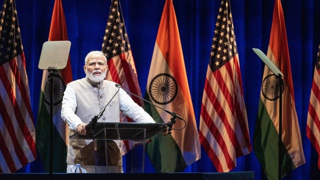 Indian PM giving a speech, US-India flags seen in the background