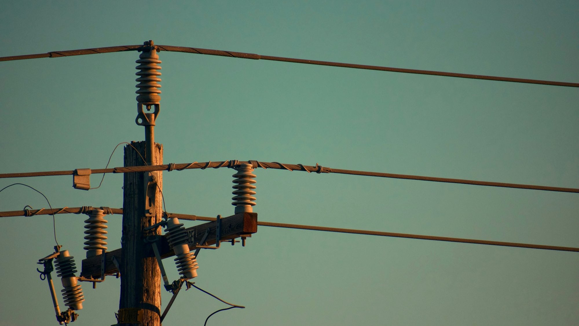 Close-up of an electricity utility pole at dusk, showing detailed components like insulators and electrical wires against a clear sky.