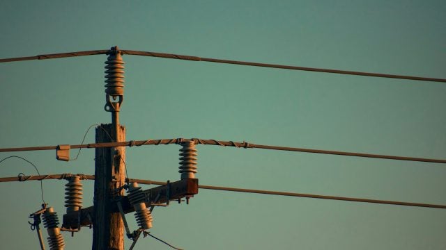 Close-up of an electricity utility pole at dusk, showing detailed components like insulators and electrical wires against a clear sky.