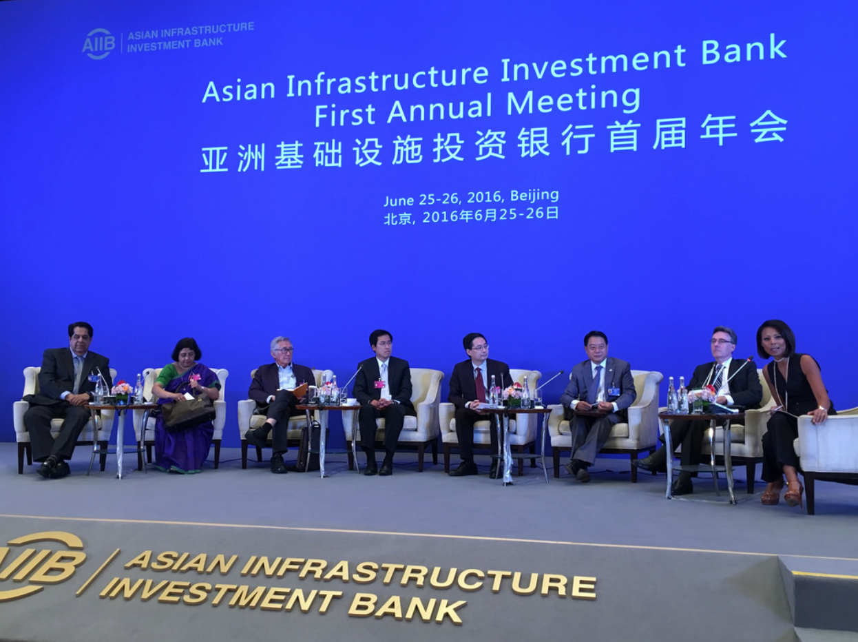 A panel of people sit on a stage in front of a screen that reads,