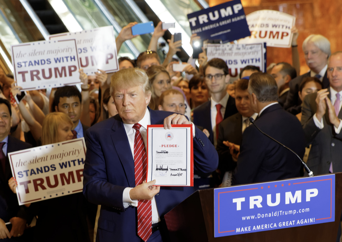 Donald Trump stands in front of a crown of supporters, holding up a signed pledge to support the Republican Party presidential candidate.
