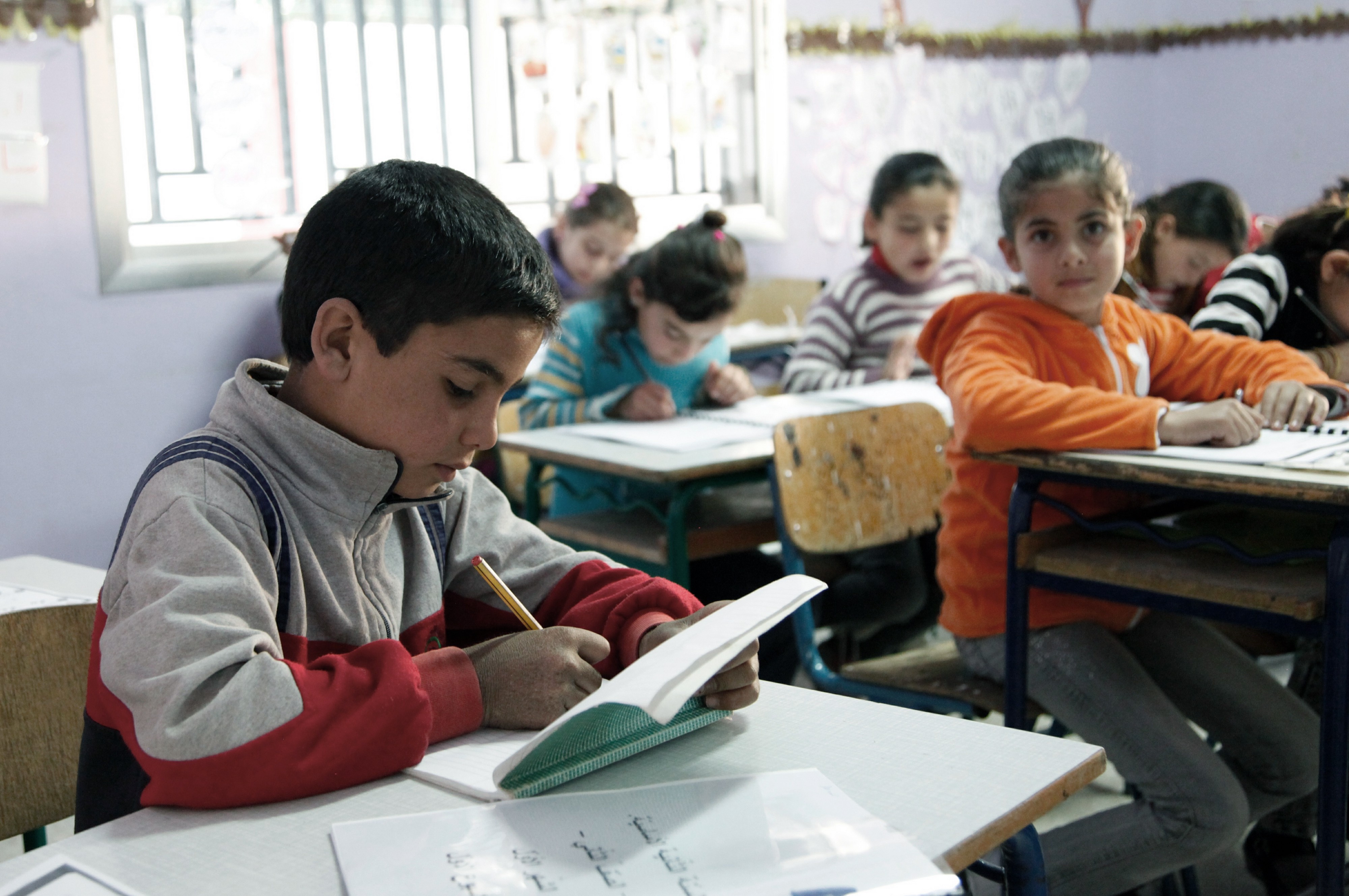 A Syrian student writes in a book in a classroom