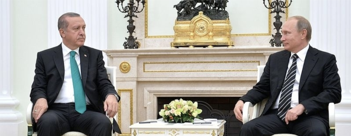 Putin and Erdogan sit in chairs in front of an ornate fireplace.