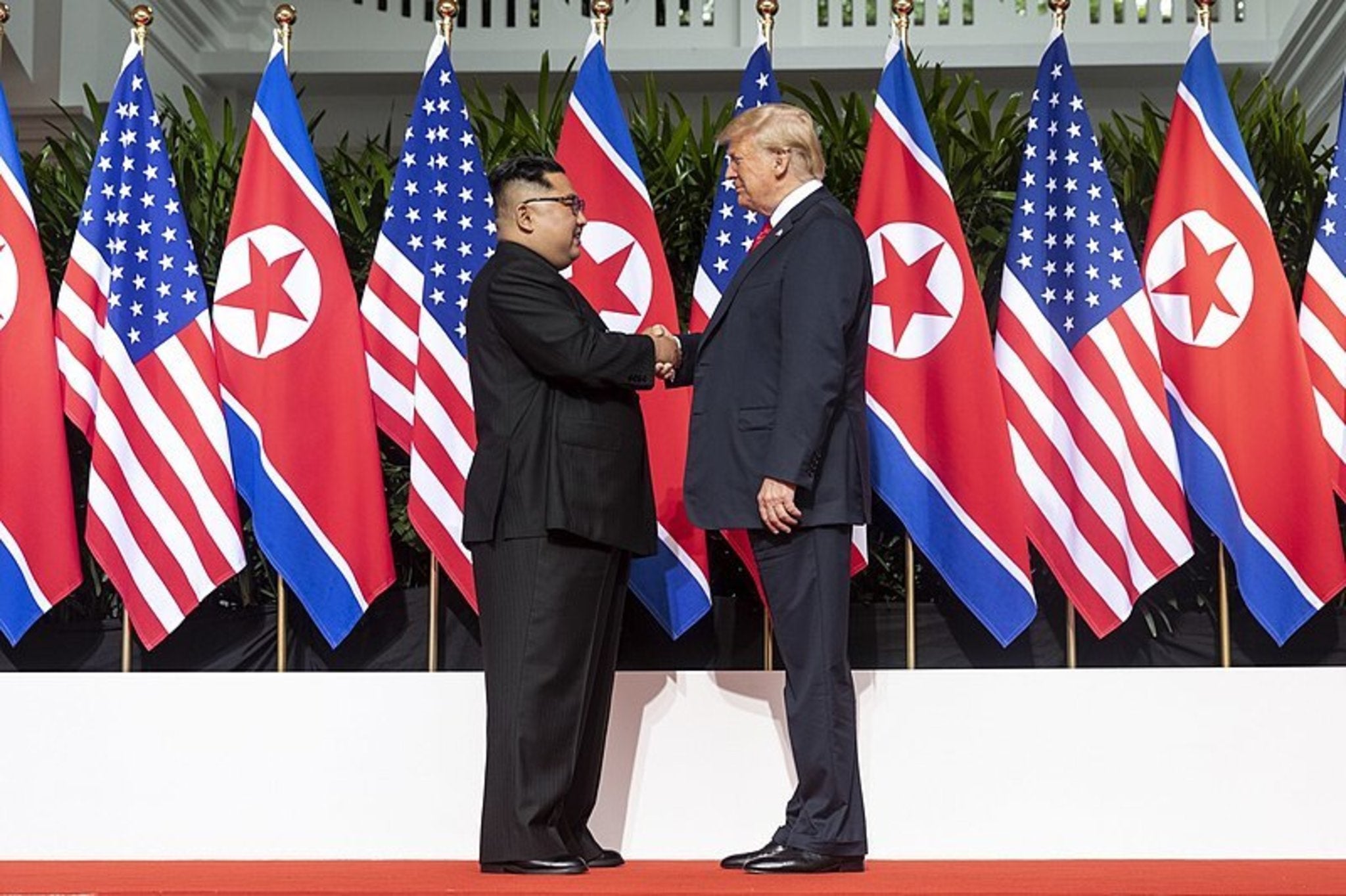 Donald trump and Kim Jong Un shanking hands in front of US and North Korean Flags