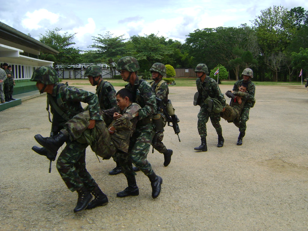 Thai soldiers practicing counterinsurgency training. Several men in Thai military uniform carrying another man in uniform.