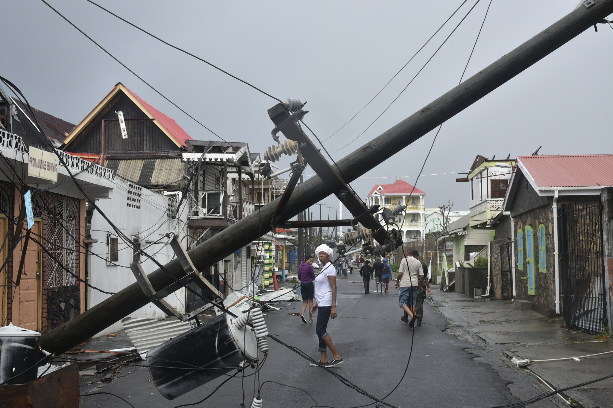 A fallen over telephone pole following natural disaster with people on the streets