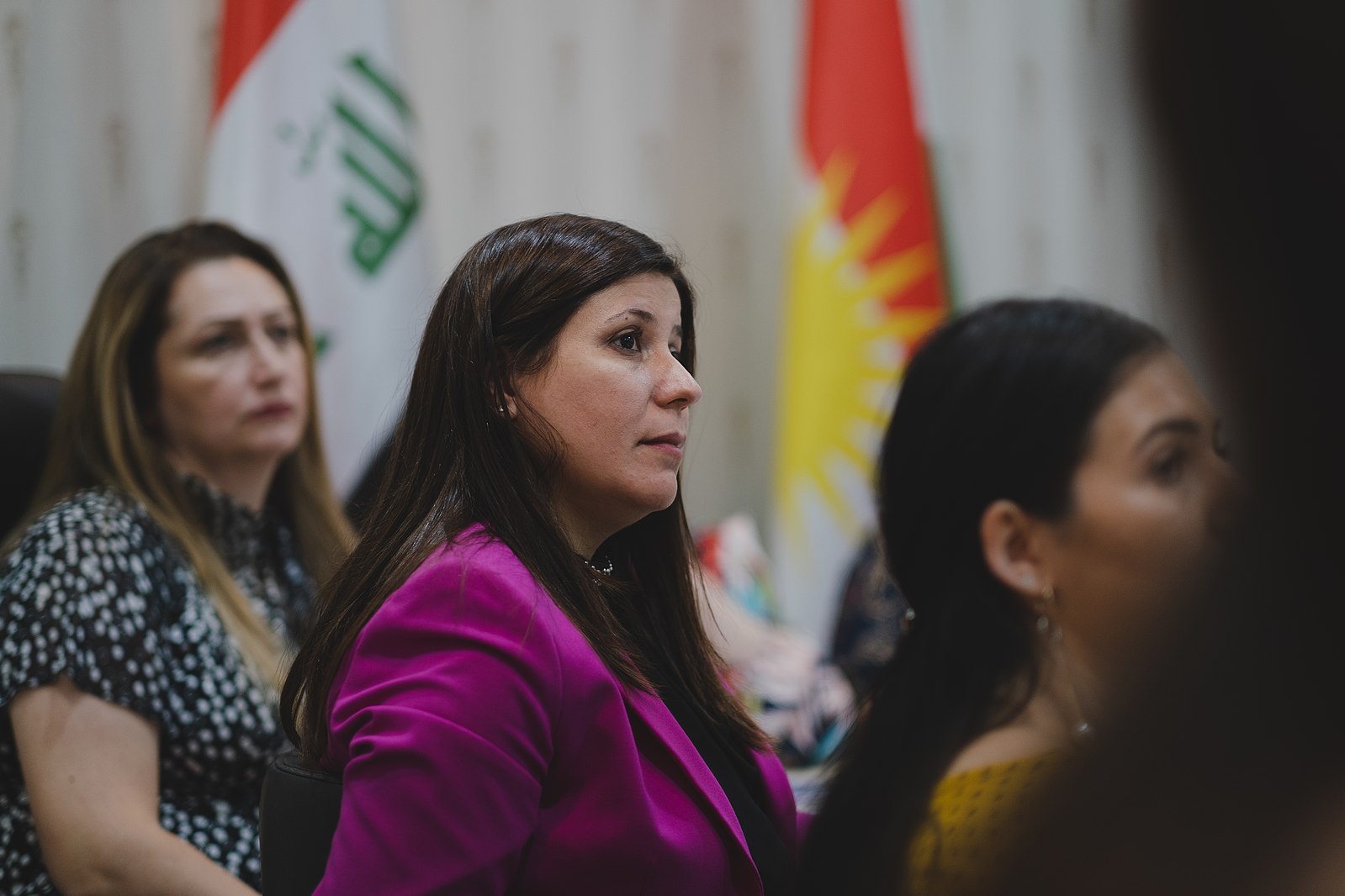 Florin Gorgis, a female human rights and women's rights activist, sits at a table looking into the distance. The flags of Kurdistan and Iraq are in the background.
