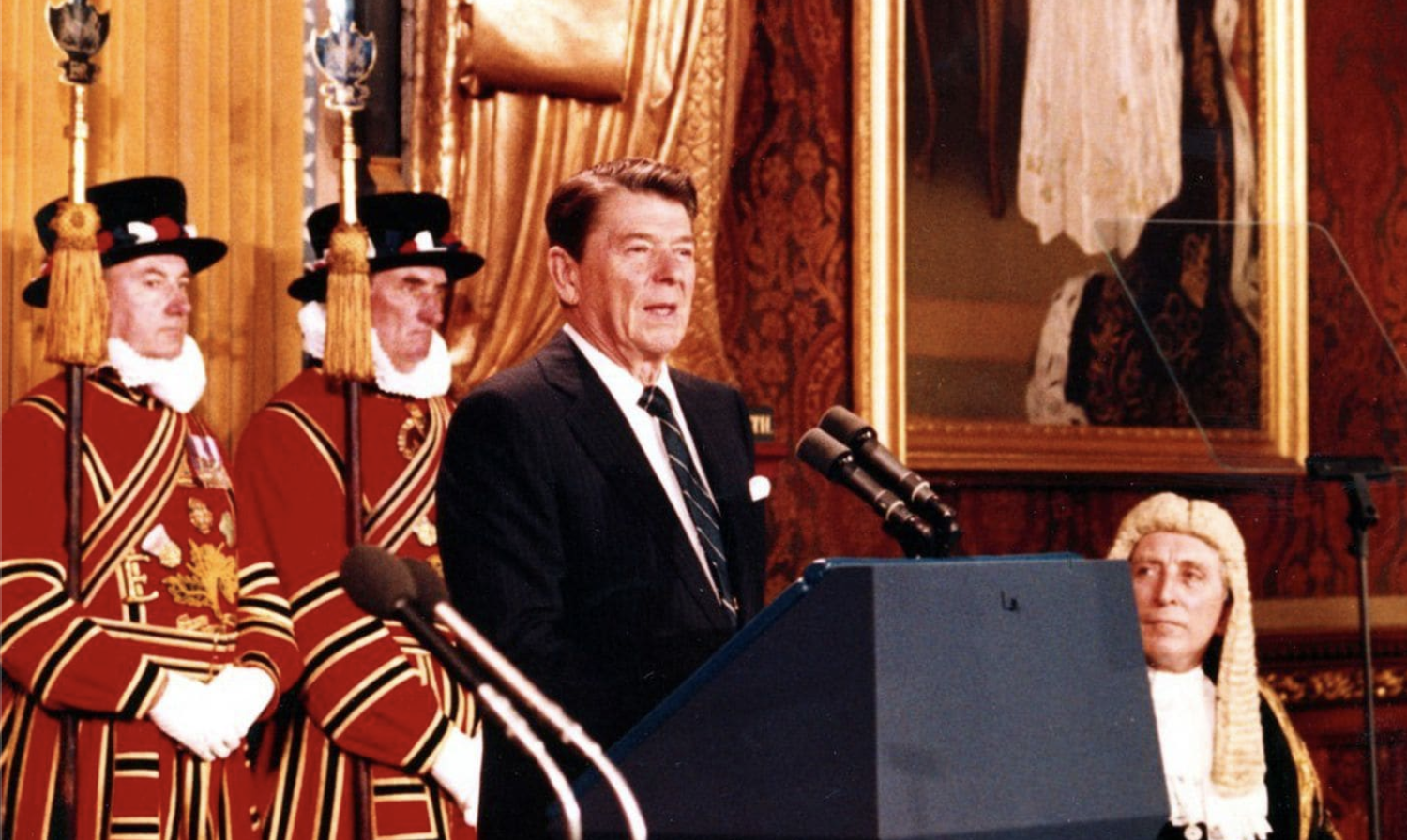 Ronald Reagan is standing at a podium and addresses the British parliament.