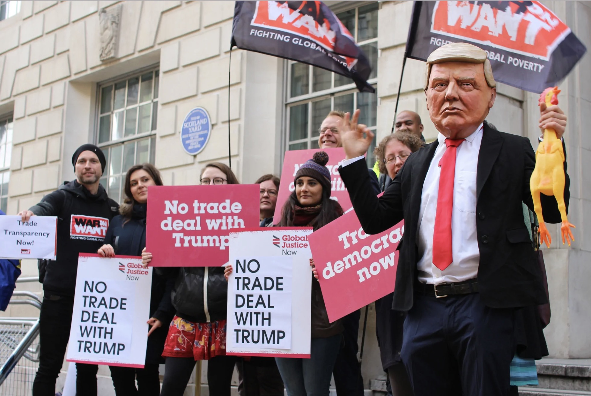 People standing outside of a building with banners and face masks protesting trump policy