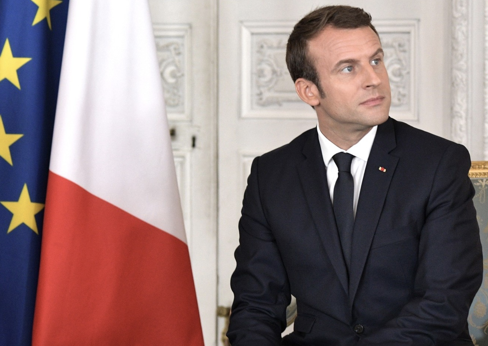 Emmanuel Macron sits in front of a French flag