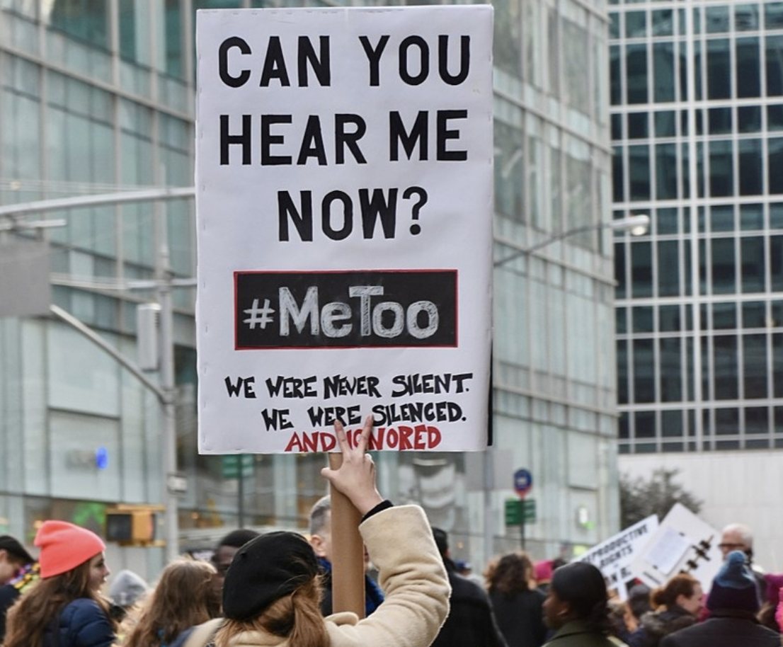 A woman stands in a crowd of protestors holding a sign that reads, 