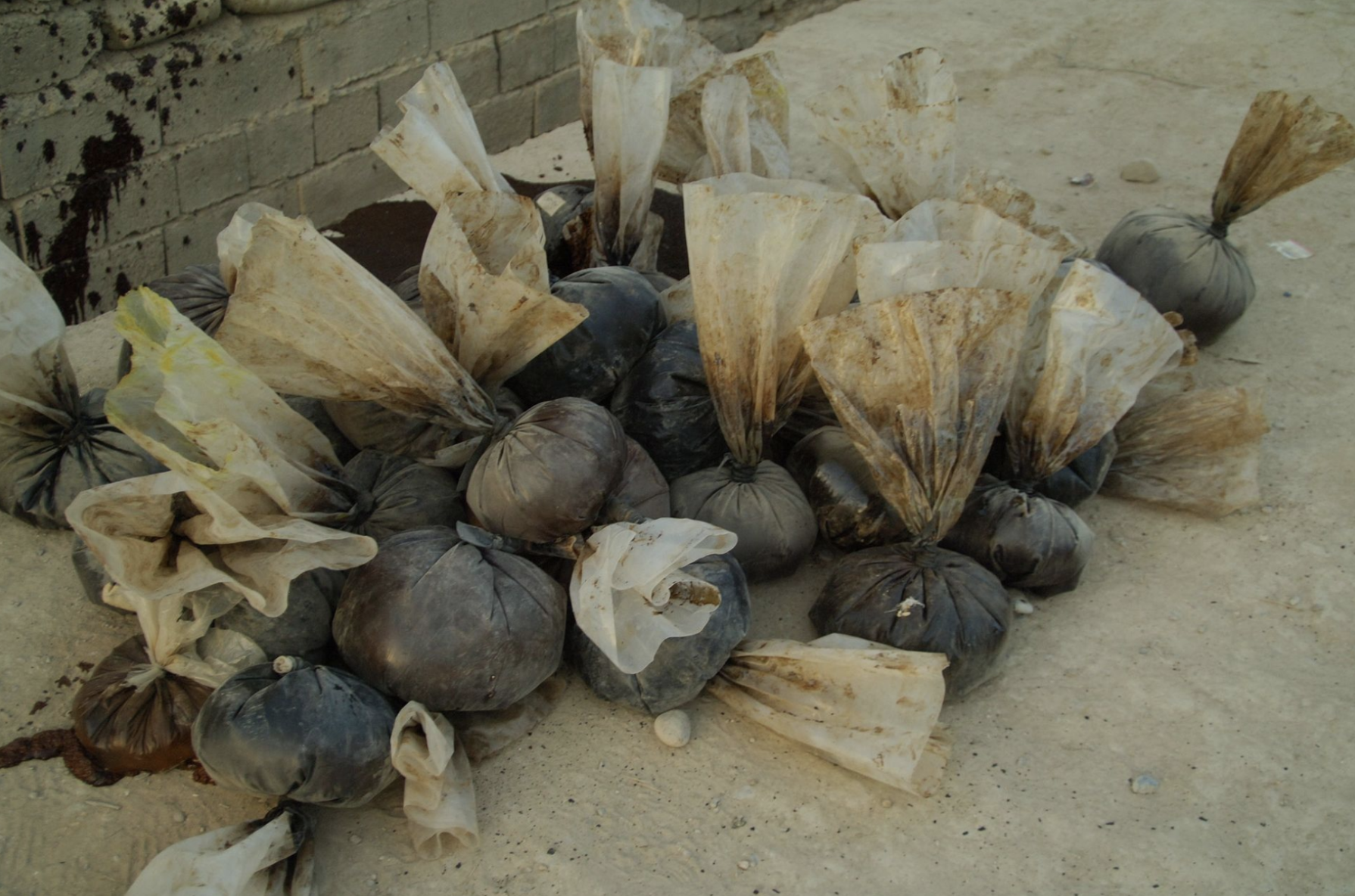 A pile of drug balloons sits on a dirt floor.
