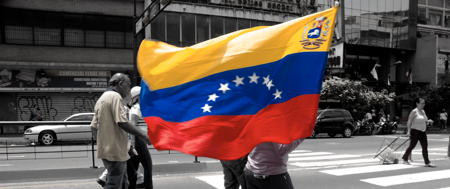 A person walks down the middle of a street carrying the Venezuelan flag.