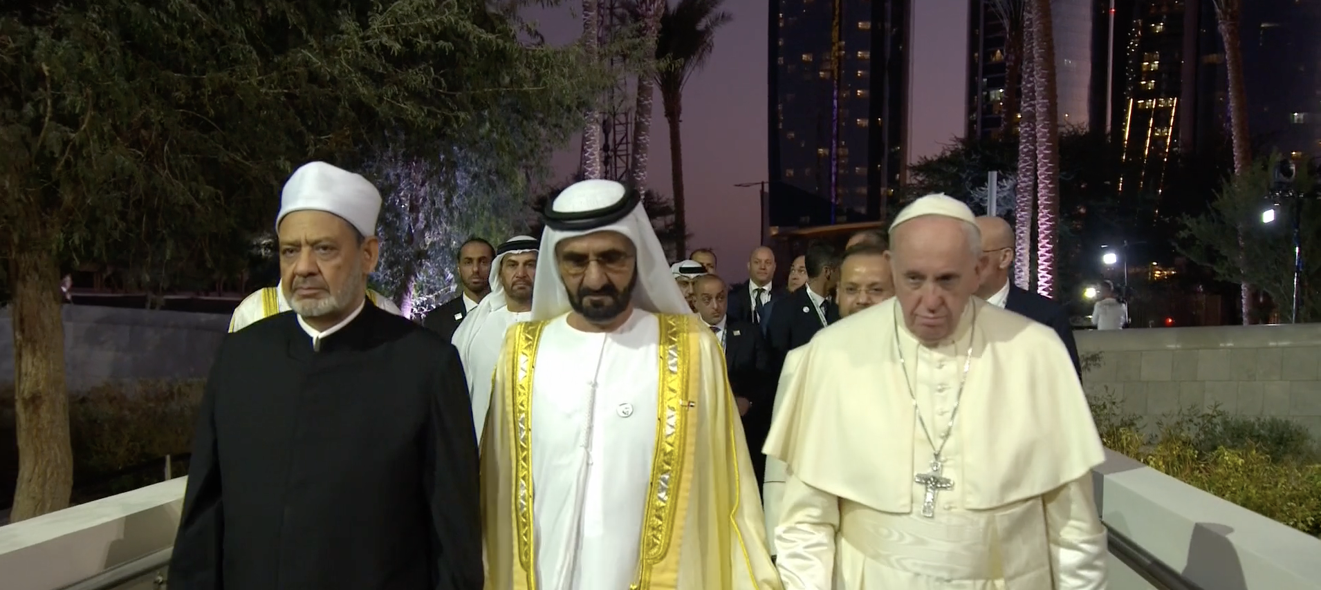 Sheikh Mohammed, Sheikh Ahmed el-Tayeb, and Pope Francis walk side-by-side in front of a crowd of people.