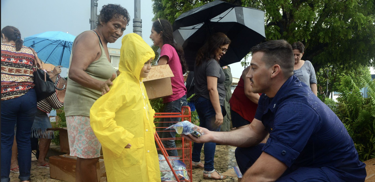 A man leans down to hand a small food and water package to a young girl.