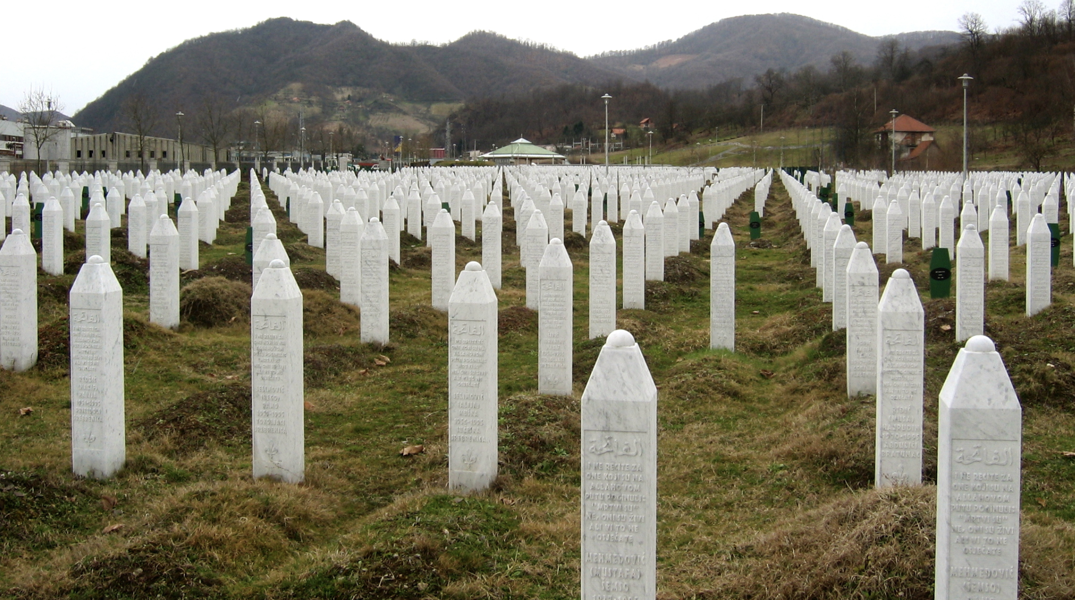 Rows of white, pillar-shaped gravestones are lined up in a field as part of a memorial to the Srebrenica genocide.