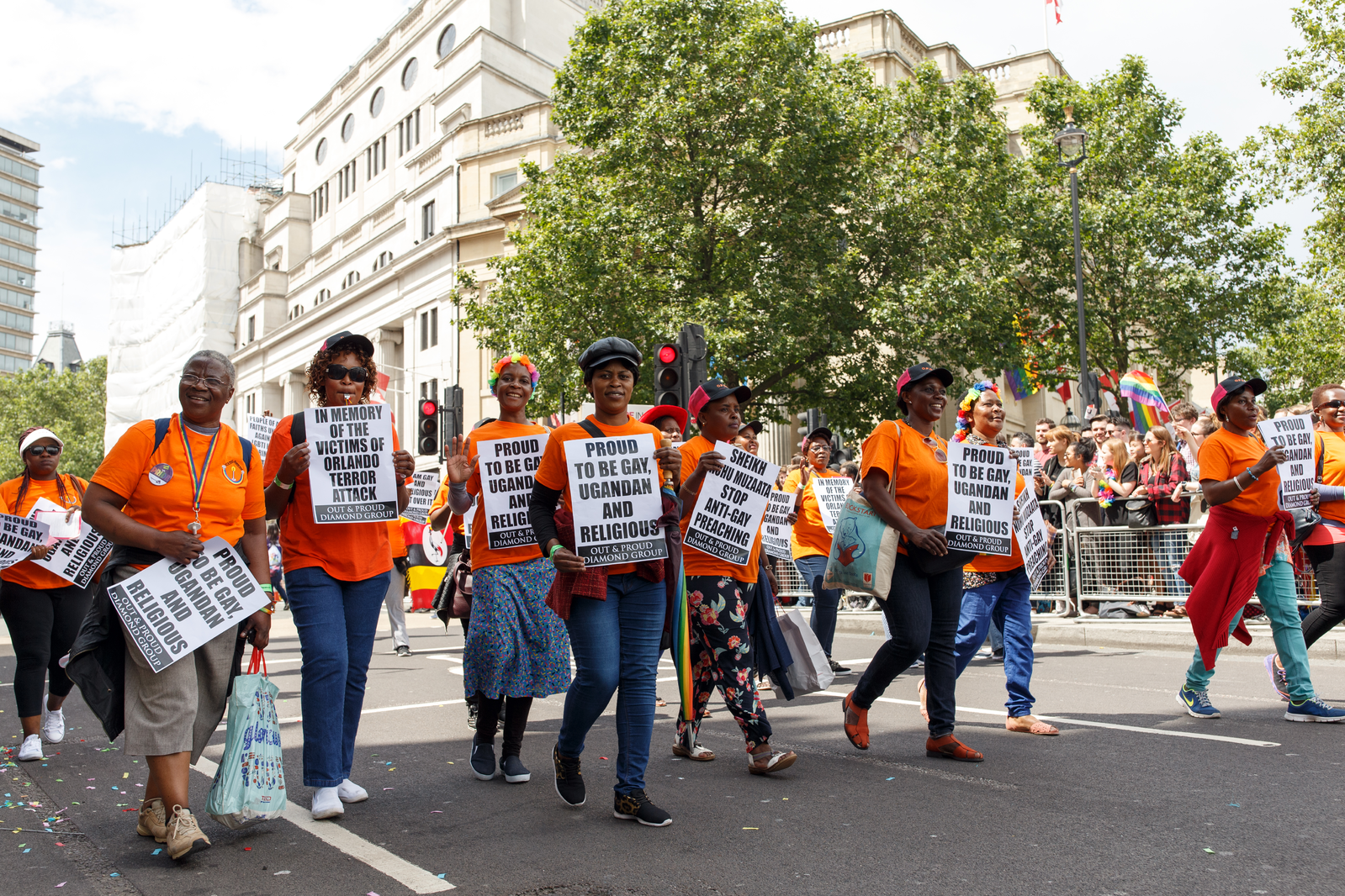 A line of people walking in a parade in Uganda holding pro-LGBTQ signs.